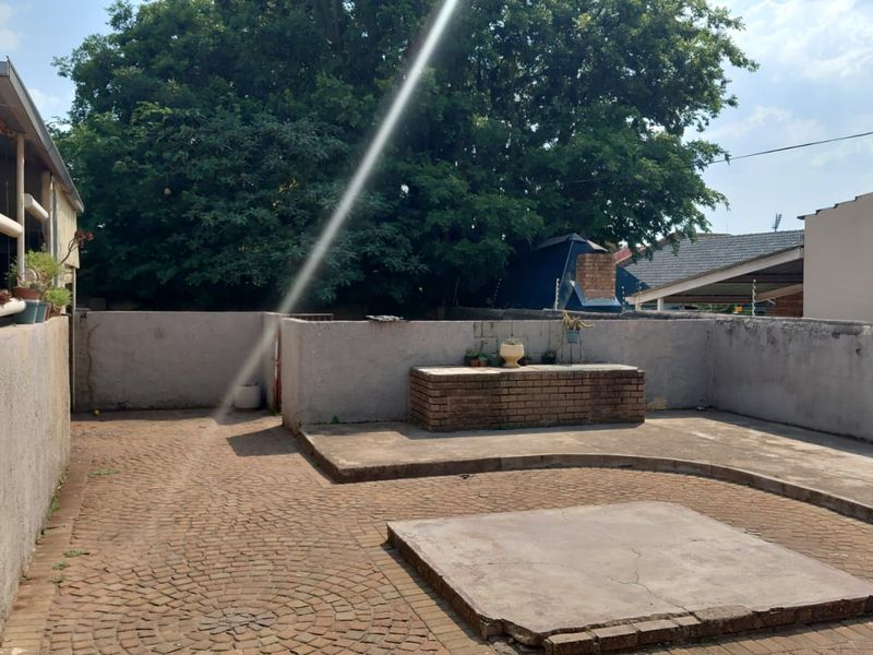 A rear courtyard featuring a paved surface, a built-in brick braai area, and perimeter boundary walls, offering potential for outdoor entertainment space.