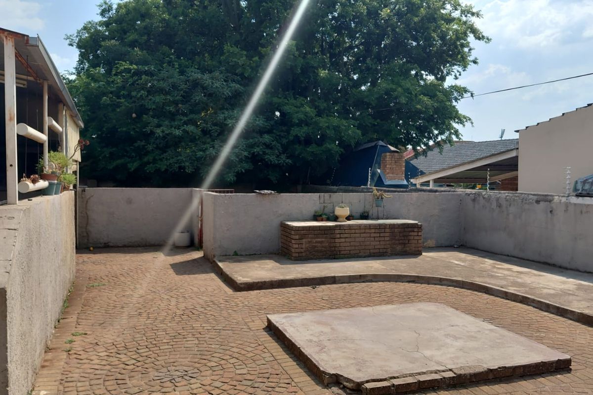 A rear courtyard featuring a paved surface, a built-in brick braai area, and perimeter boundary walls, offering potential for outdoor entertainment space.