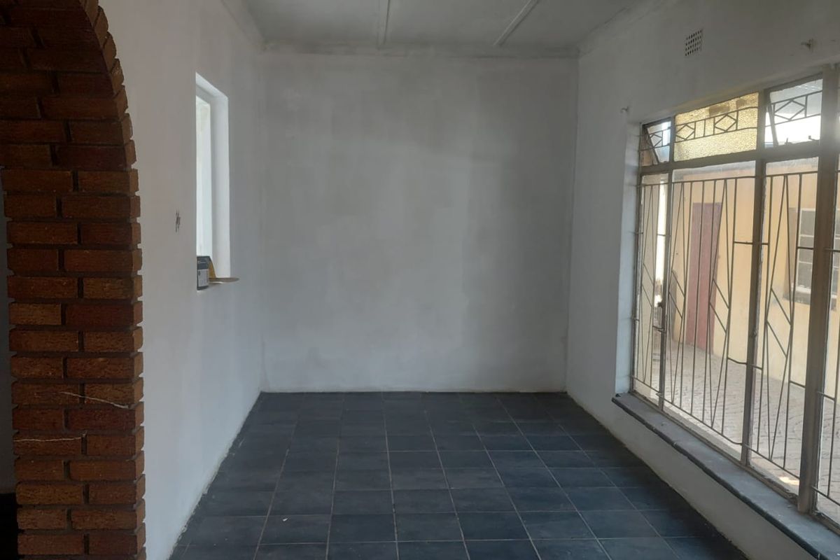 An empty living area featuring dark tiled flooring, a distinctive brick archway, and large windows with integrated metal security bars.