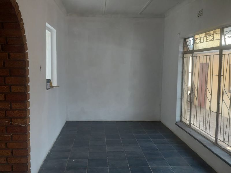An empty living area featuring dark tiled flooring, a distinctive brick archway, and large windows with integrated metal security bars.