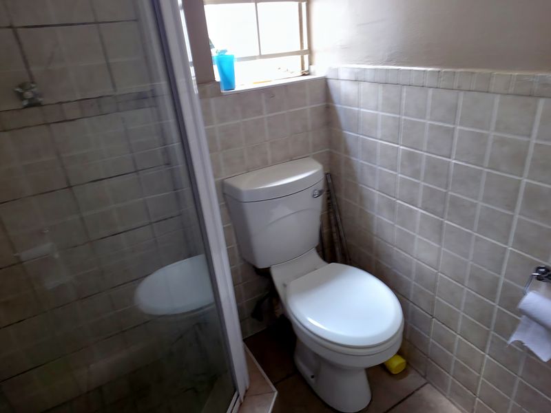 A compact bathroom featuring a shower enclosure, toilet, and neutral tiled finishes throughout.