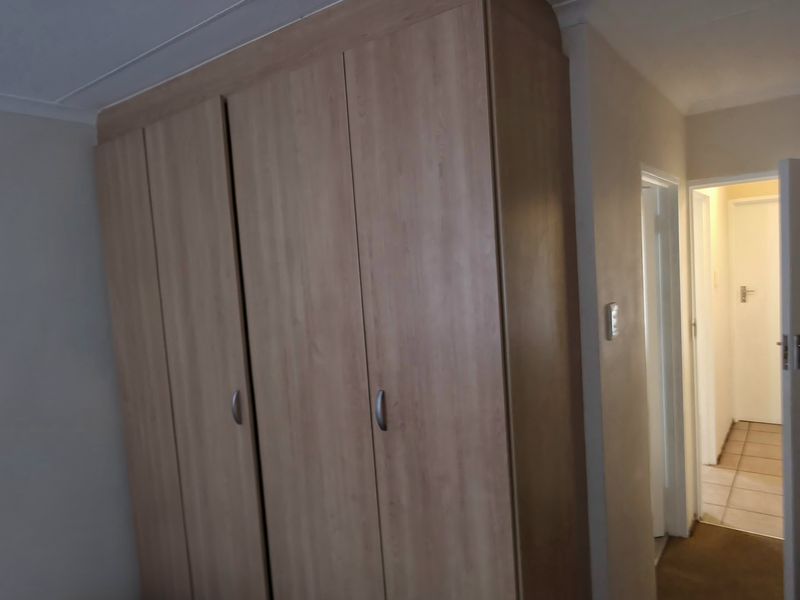 A bedroom featuring a large built-in wooden wardrobe and access to an adjoining hallway.