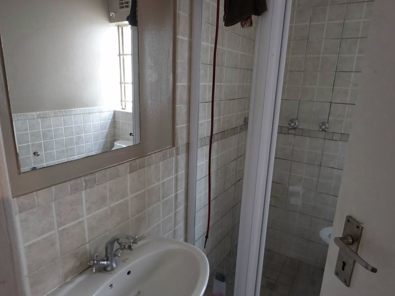A functional bathroom featuring a pedestal basin, wall-mounted mirror, and a separate shower enclosure with tiled walls.