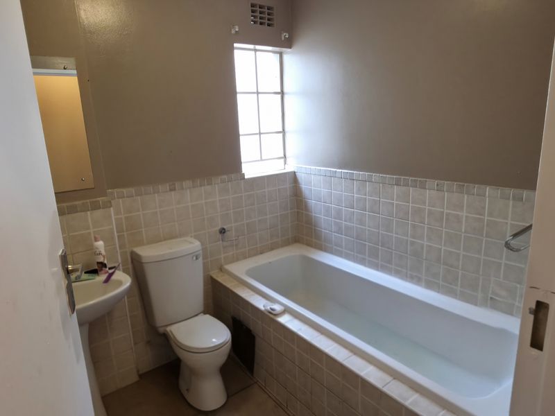 A compact bathroom featuring a bathtub, pedestal basin, and toilet with neutral wall tiles and a security-grille window.
