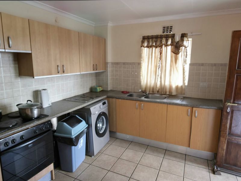 Functional kitchen featuring laminate cabinetry, built-in oven, electric hob, and double bowl sink with tiled splashback and ceramic flooring.