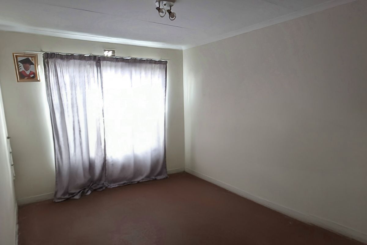 A simple, empty bedroom featuring neutral walls, carpeted flooring, and a window with curtains.