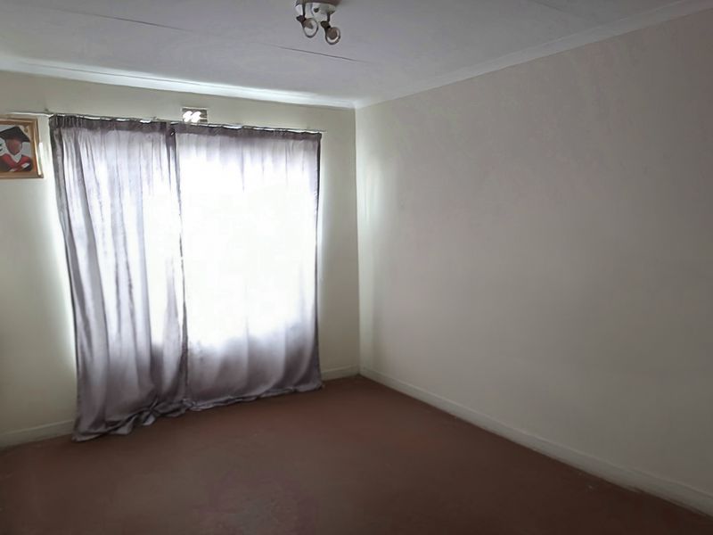 A simple, empty bedroom featuring neutral walls, carpeted flooring, and a window with curtains.