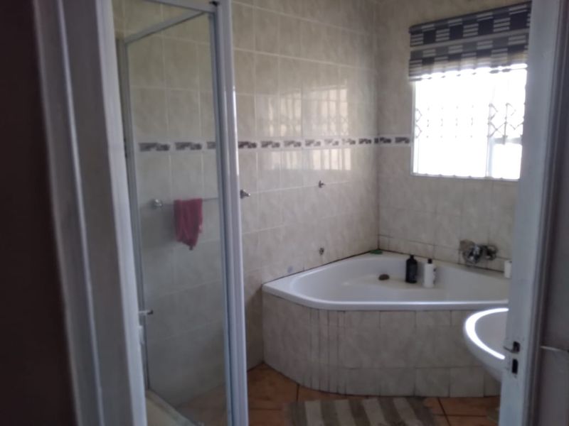 A functional bathroom featuring a corner bathtub, a separate shower enclosure, and tiled finishes throughout.