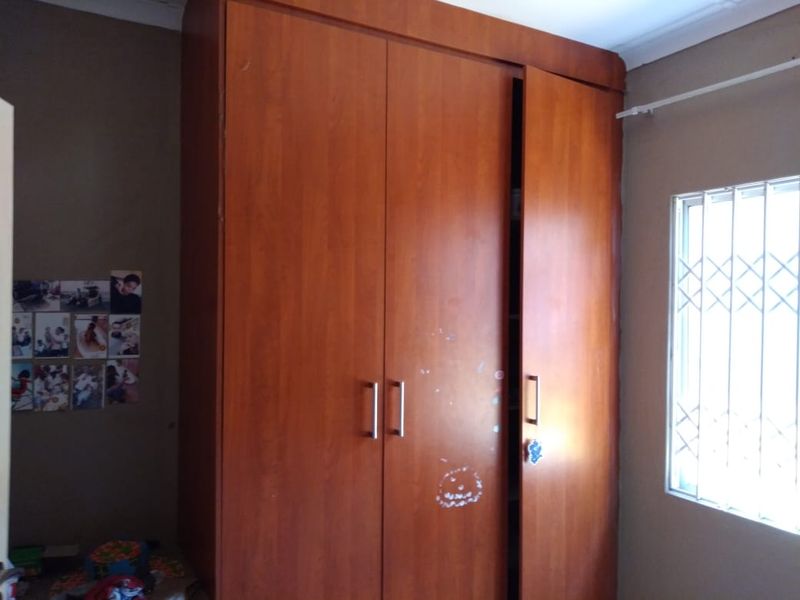 A bedroom featuring a large built-in wooden wardrobe and a window fitted with security bars.