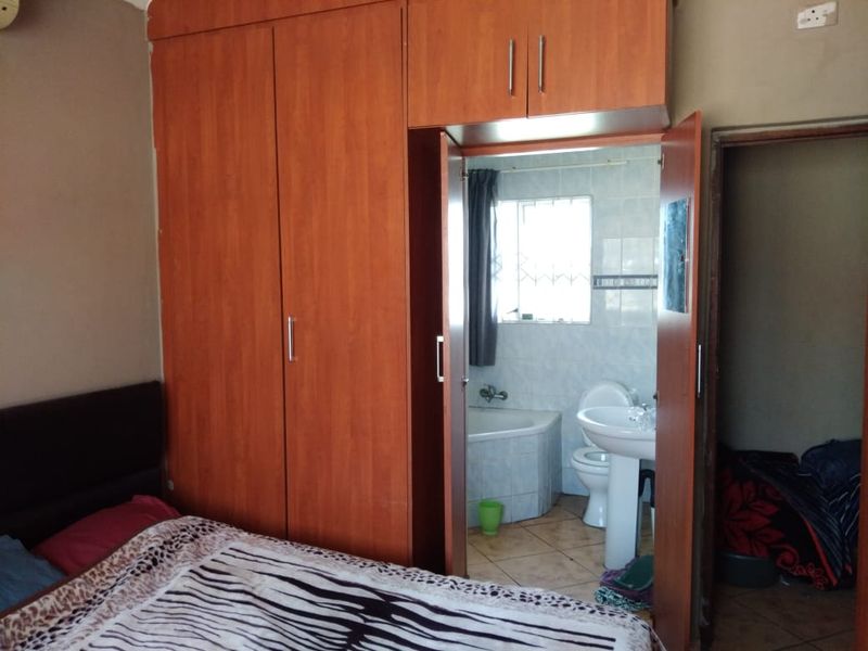 Bedroom featuring built-in wooden wardrobes and an attached en-suite bathroom equipped with a pedestal basin, toilet, and corner bathtub.
