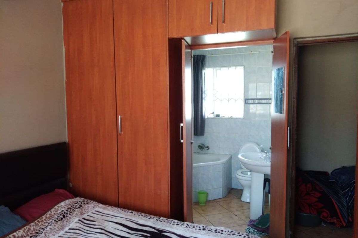 Bedroom featuring built-in wooden wardrobes and an attached en-suite bathroom equipped with a pedestal basin, toilet, and corner bathtub.