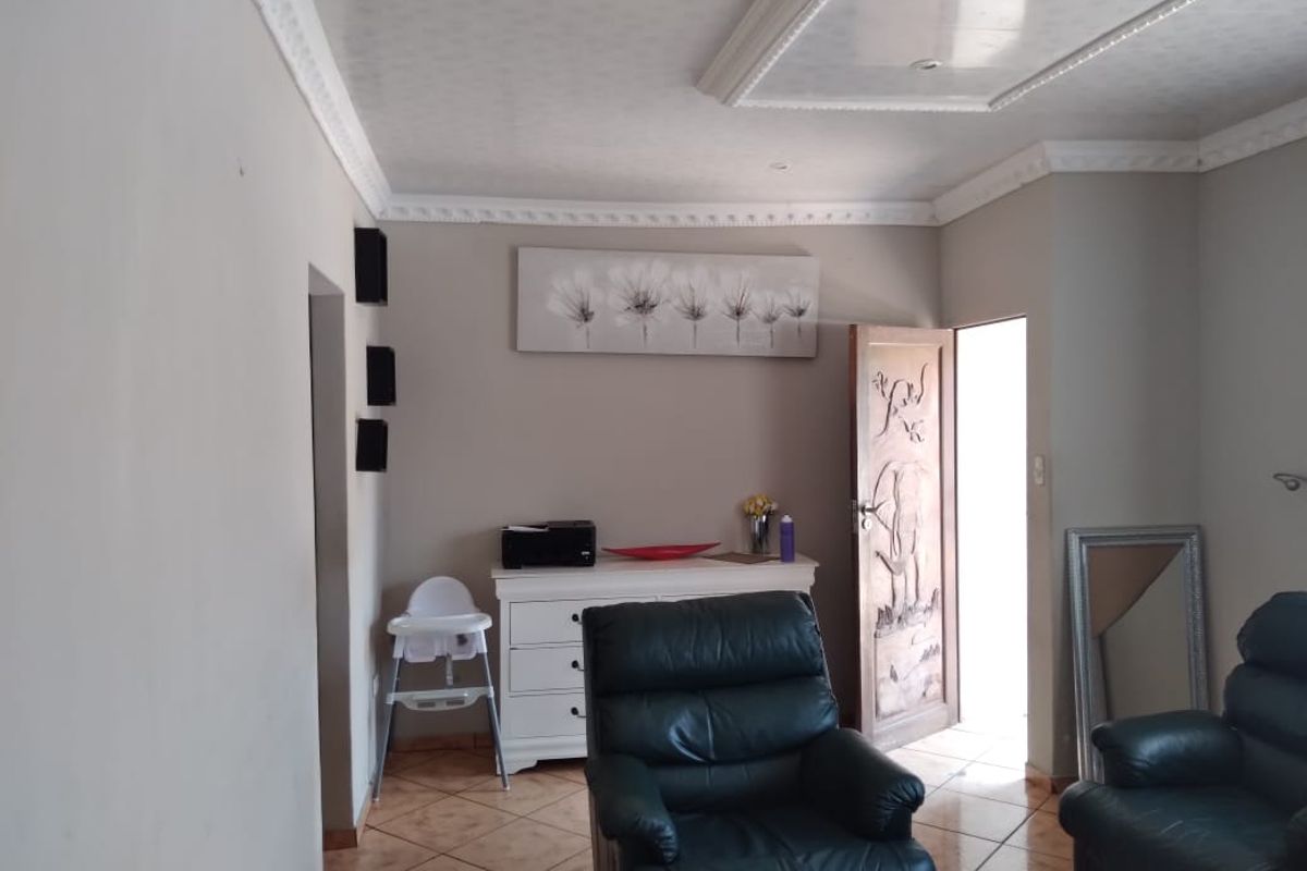 A living room featuring tiled flooring, decorative ceiling cornicing, and a unique carved wooden door leading to an exterior space.
