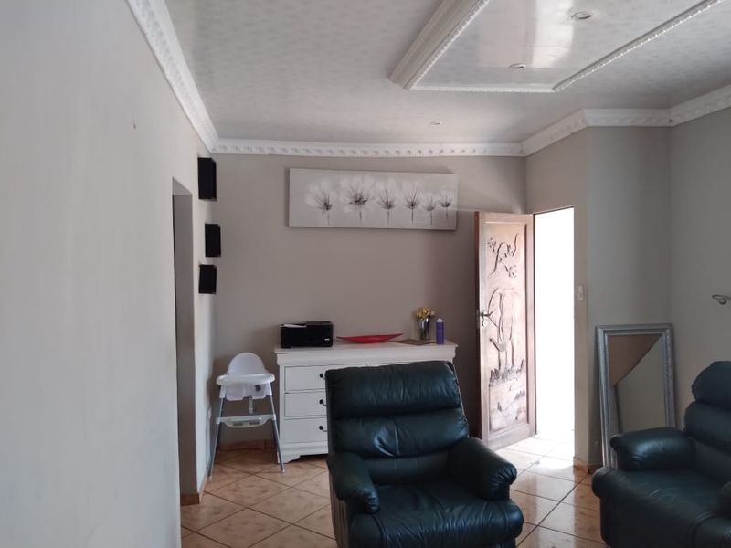 A living room featuring tiled flooring, decorative ceiling cornicing, and a unique carved wooden door leading to an exterior space.