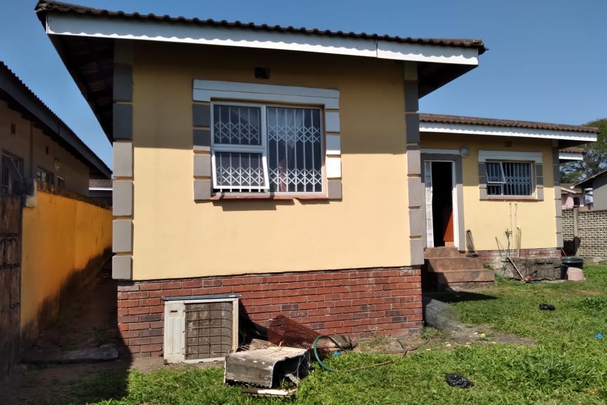Rear view of a single-story house featuring a brick plinth, tiled roof, and security bars on windows, set within a grassed yard area.
