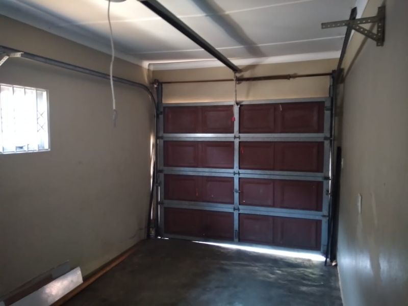 An empty single garage space featuring a sectional door, security-barred window, and basic concrete flooring, suitable for vehicle storage or workshop conversion.