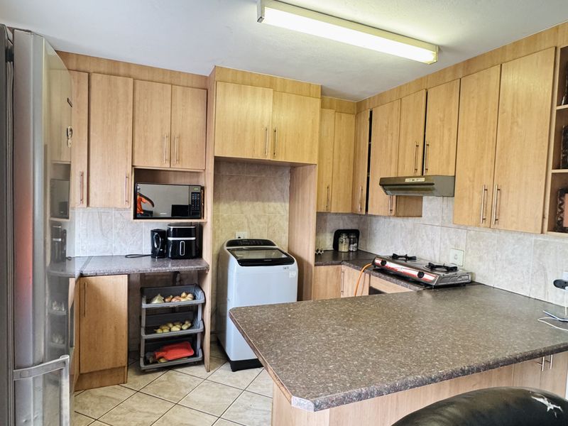 A functional kitchen featuring light wood-tone cabinetry, laminate countertops, tiled backsplash, and tiled flooring with an integrated extractor fan and stove.