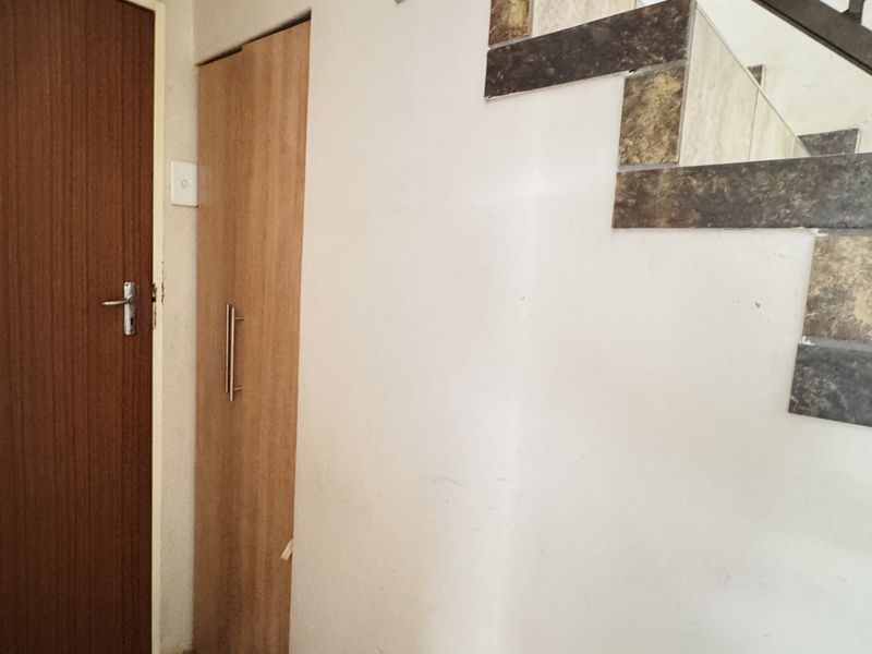 A functional hallway area featuring a staircase with decorative tiled accents, a built-in storage cupboard, and tiled flooring.