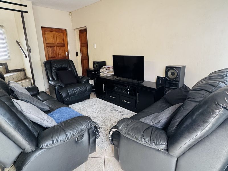A living room featuring tiled flooring and a staircase, showing signs of wear on the walls and ceiling.