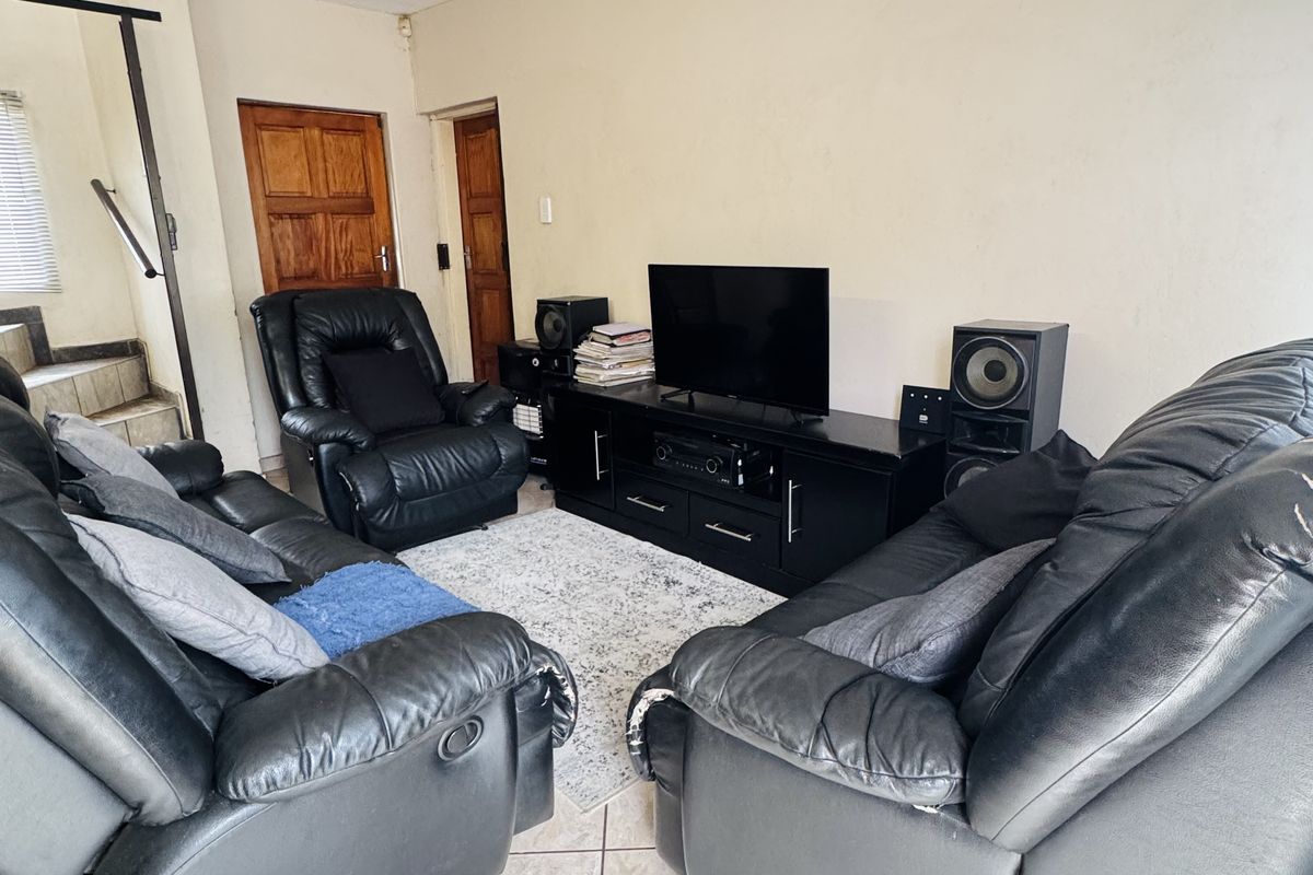 A living room featuring tiled flooring and a staircase, showing signs of wear on the walls and ceiling.