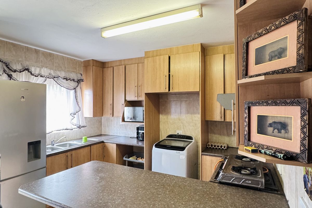 A functional kitchen featuring laminate cabinetry, ample counter space, a double basin sink, and a built-in hob with tiled finishes.