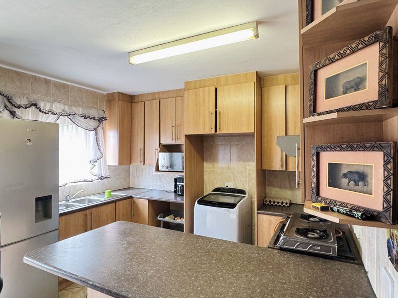 A functional kitchen featuring laminate cabinetry, ample counter space, a double basin sink, and a built-in hob with tiled finishes.