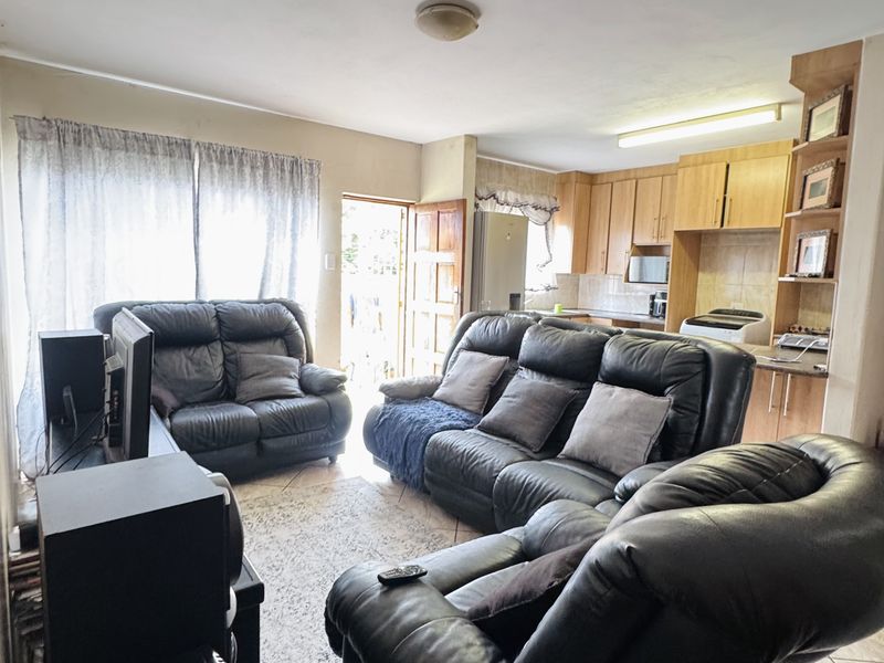Open plan living area featuring tiled floors and a functional kitchen with built-in cabinetry and shelving, offering a practical layout for daily living.