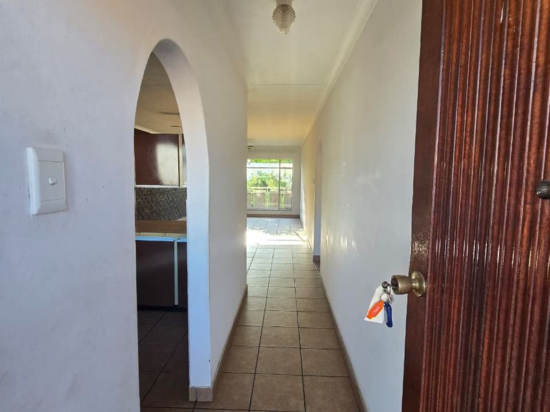 A tiled hallway featuring an arched entryway leading to the living area, with a wooden door and neutral wall finishes.