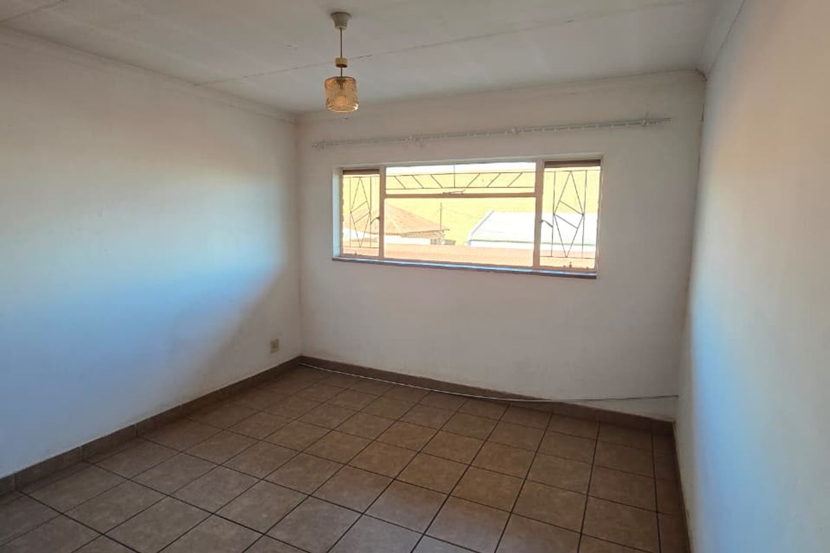 An empty bedroom featuring tiled flooring, a metal-framed window with security bars, and a central ceiling light fixture.