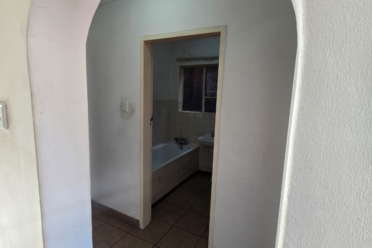 A view through an arched doorway into a functional bathroom featuring tiled flooring, a bathtub, and a washbasin.