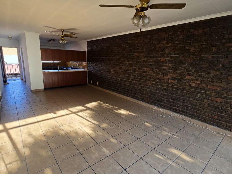 Spacious open-plan living and kitchen area featuring tiled flooring, a prominent exposed brick wall, and ceiling fans, offering a versatile layout.