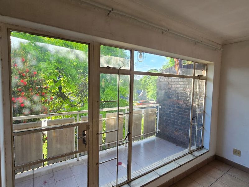 An empty living area featuring tiled flooring and large glass doors providing direct access to a private balcony with outdoor views.