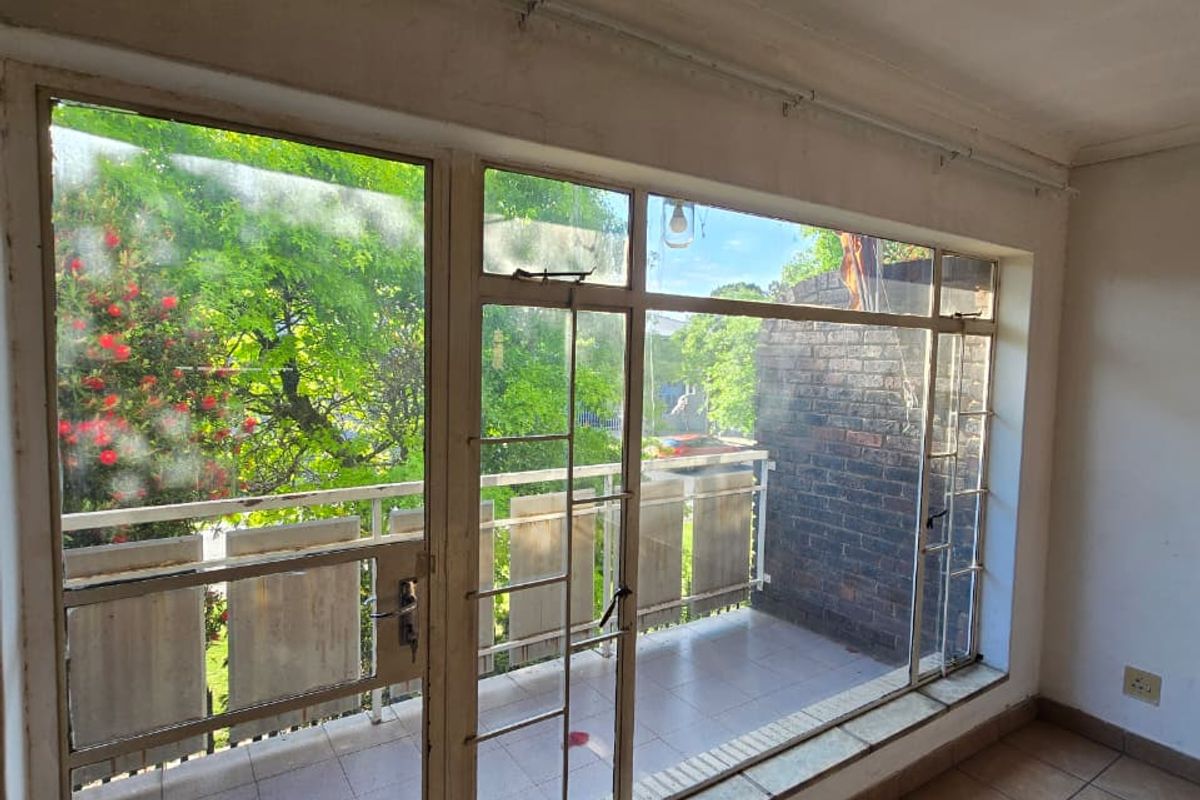 An empty living area featuring tiled flooring and large glass doors providing direct access to a private balcony with outdoor views.