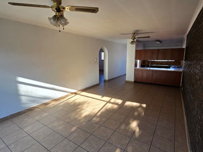 Spacious open-plan living and kitchen area featuring tiled floors, an exposed brick feature wall, and classic ceiling fans.
