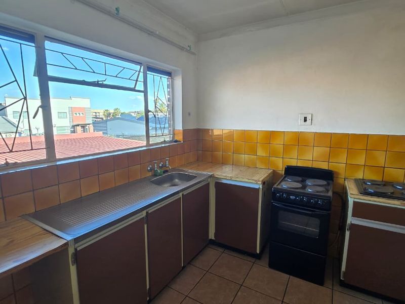 A dated kitchen featuring original cabinetry, tiled backsplash, and tiled flooring, offering a functional layout ready for modernization and renovation.
