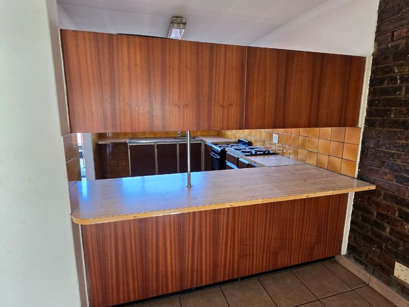 A functional kitchen featuring a breakfast bar, built-in wooden cabinetry, gas hob, oven, and an exposed brick feature wall with tiled flooring.