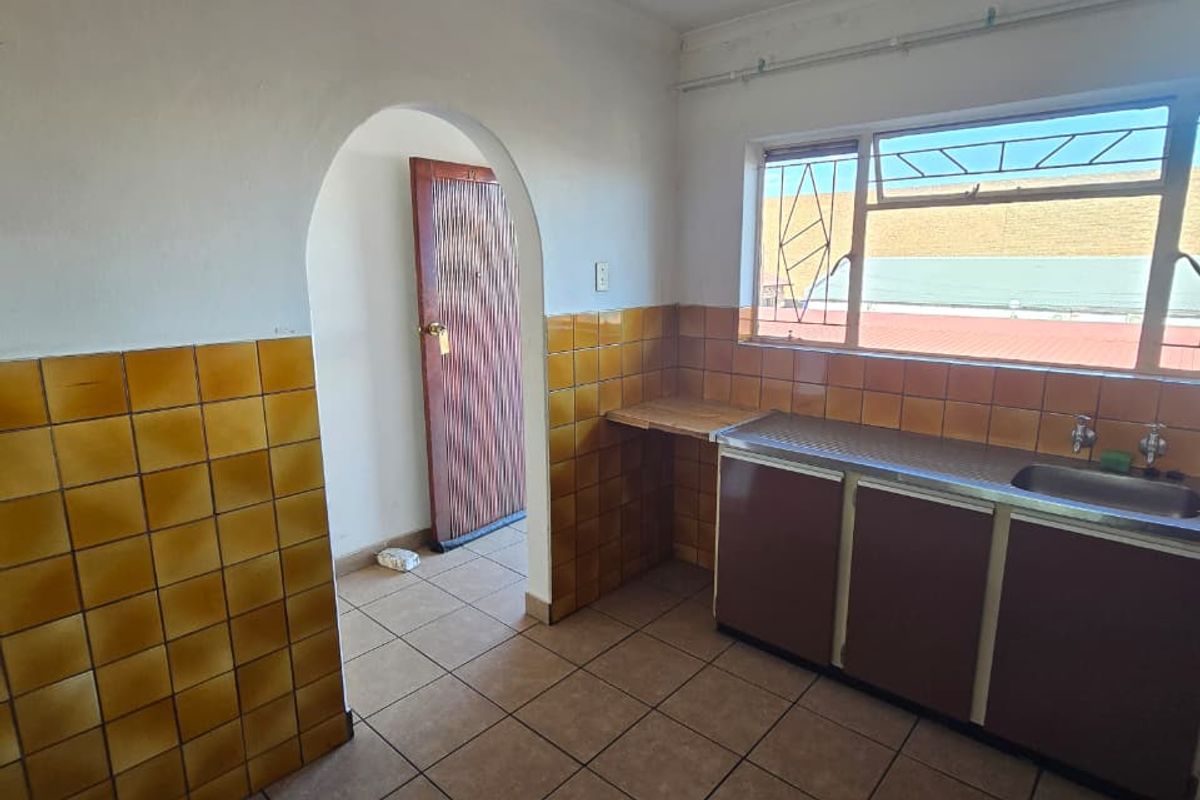 A dated kitchen featuring tiled walls, built-in cabinetry with a stainless steel sink, and tiled flooring, accessible via a classic arched doorway.