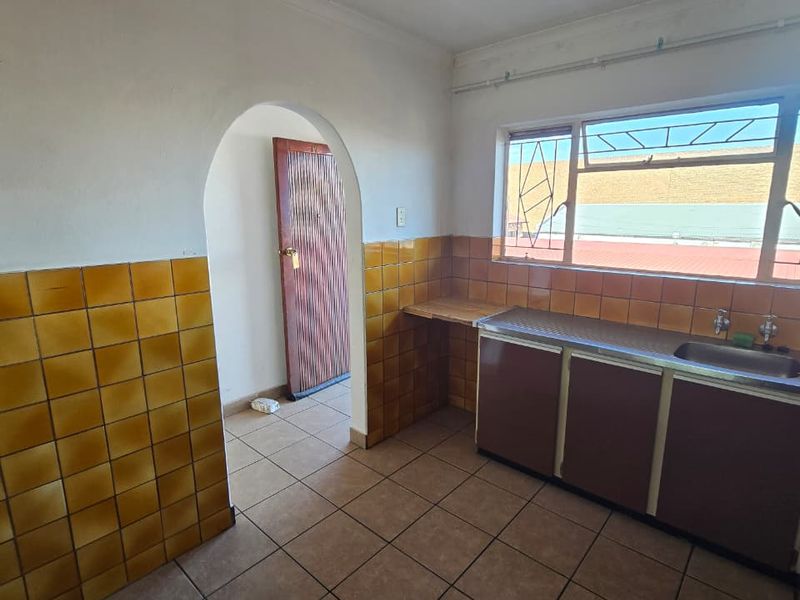 A dated kitchen featuring tiled walls, built-in cabinetry with a stainless steel sink, and tiled flooring, accessible via a classic arched doorway.