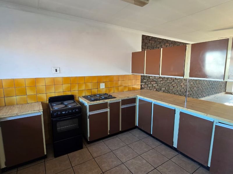 A dated kitchen featuring brown cabinetry, yellow tiled backsplash, tiled flooring, and a freestanding stove, offering significant potential for modern renovation.