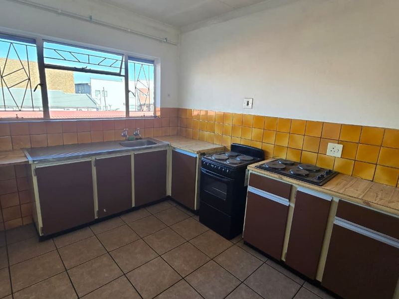 A functional kitchen featuring tiled flooring, a tiled splashback, built-in cabinetry, a stainless steel sink, and a freestanding stove with a built-in hob.