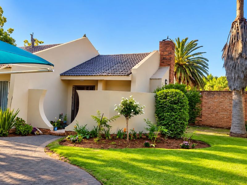 Front view of the property featuring a paved driveway, landscaped garden, brick chimney, and a shade sail over the entrance area.