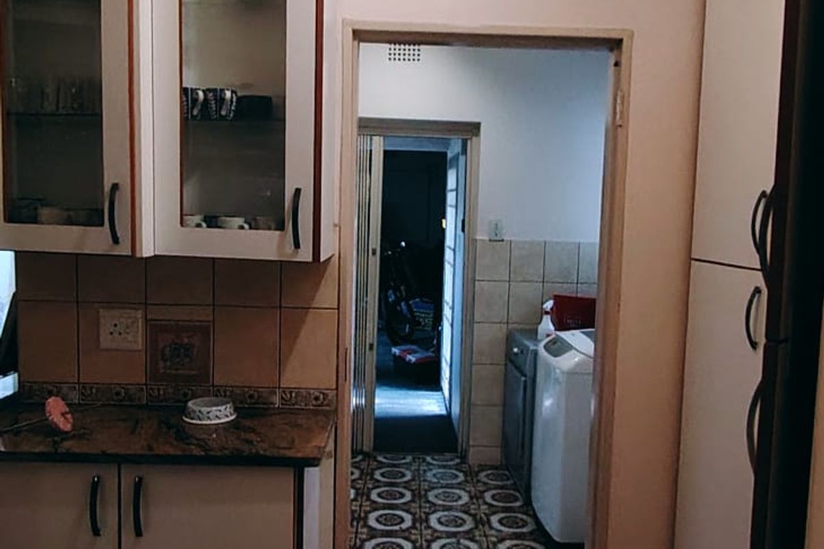 A functional kitchen featuring built-in cabinetry with granite countertops and a tiled backsplash, leading through to a separate laundry area.