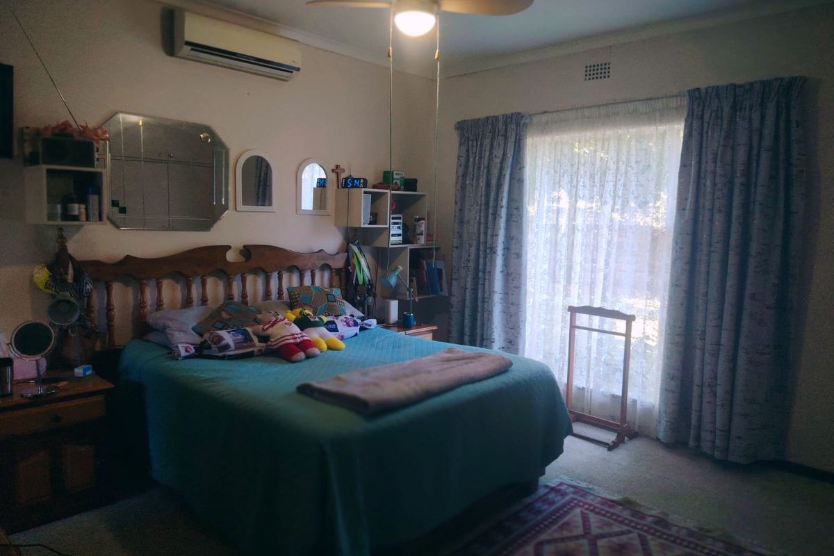 A standard bedroom featuring a ceiling fan, wall-mounted air conditioning unit, and large window with curtain tracks, offering a functional living space.