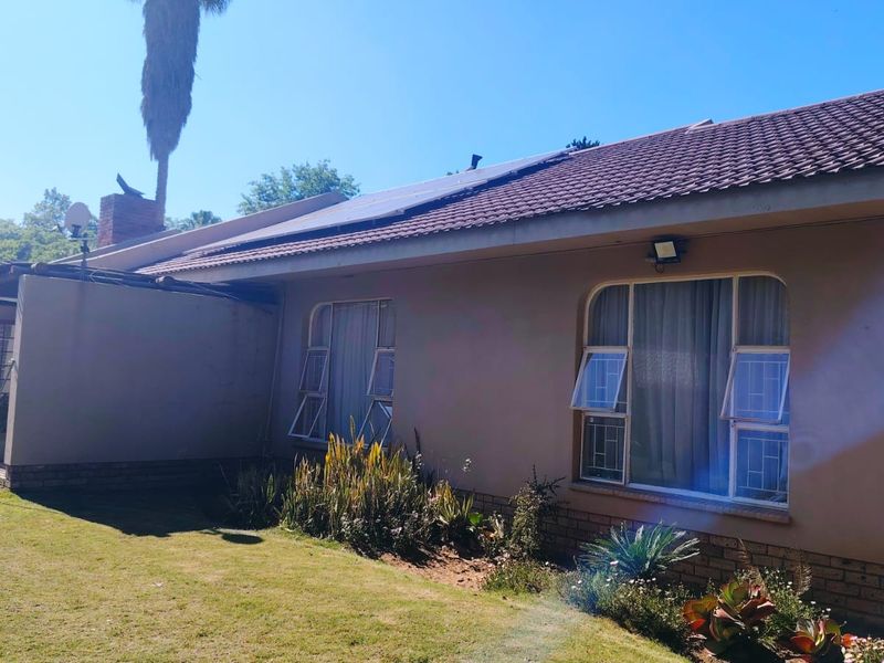 Rear view of the house featuring a tiled roof with solar panels, steel-framed windows with security bars, and a well-maintained garden area.