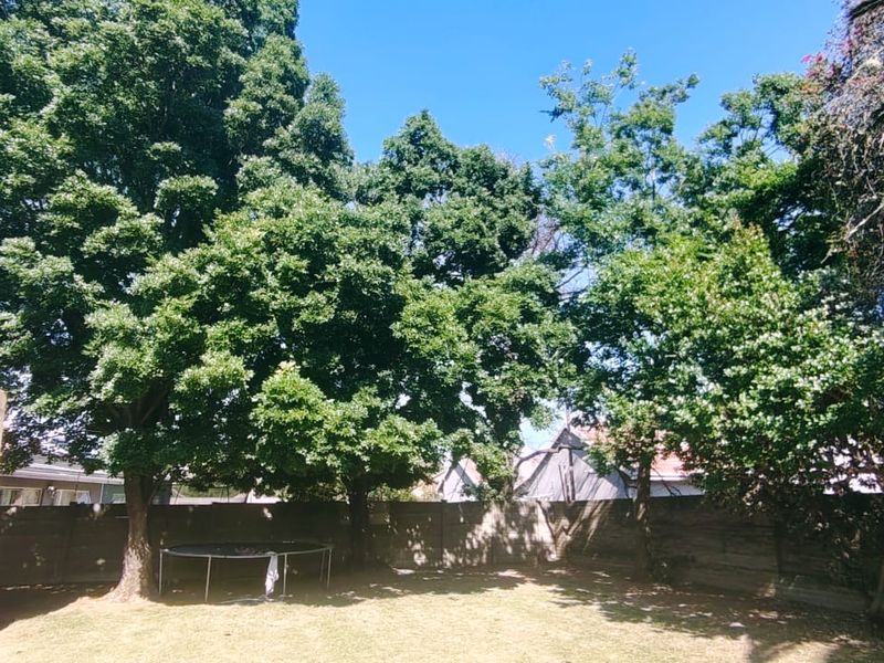 A spacious private garden featuring a well-maintained lawn, mature trees, and a secure precast concrete boundary wall.