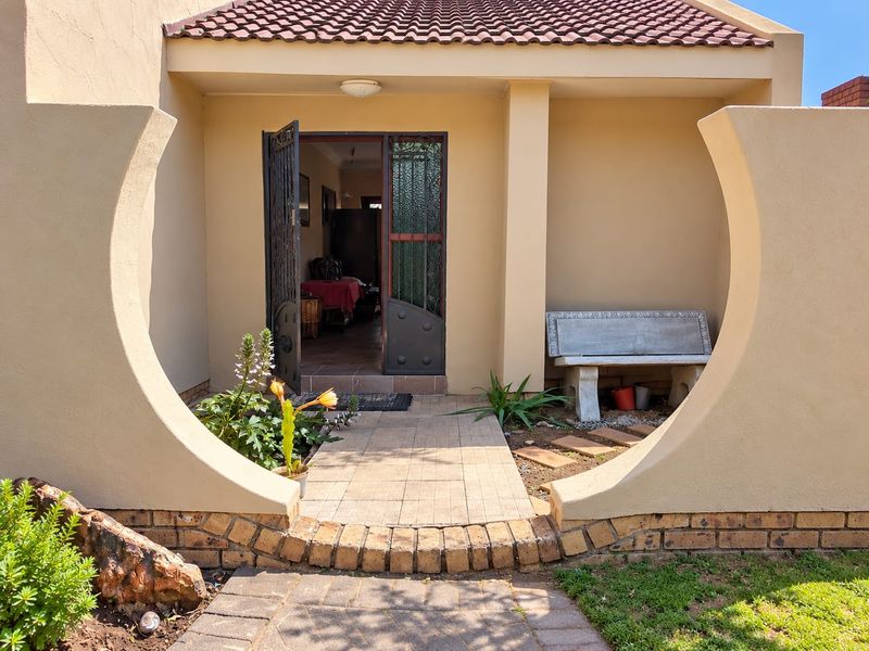 Front entrance featuring a covered porch, decorative curved masonry walls, a tiled walkway, and a secure wrought iron gate.