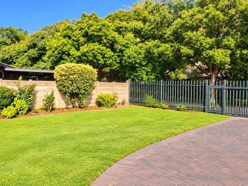 A well-maintained front garden featuring a paved driveway, manicured lawn, and secure metal gate with precast concrete boundary walling.