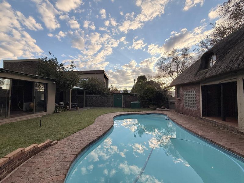 Outdoor pool area featuring a swimming pool with brick paving, surrounded by a garden and a structure with a traditional thatched roof.