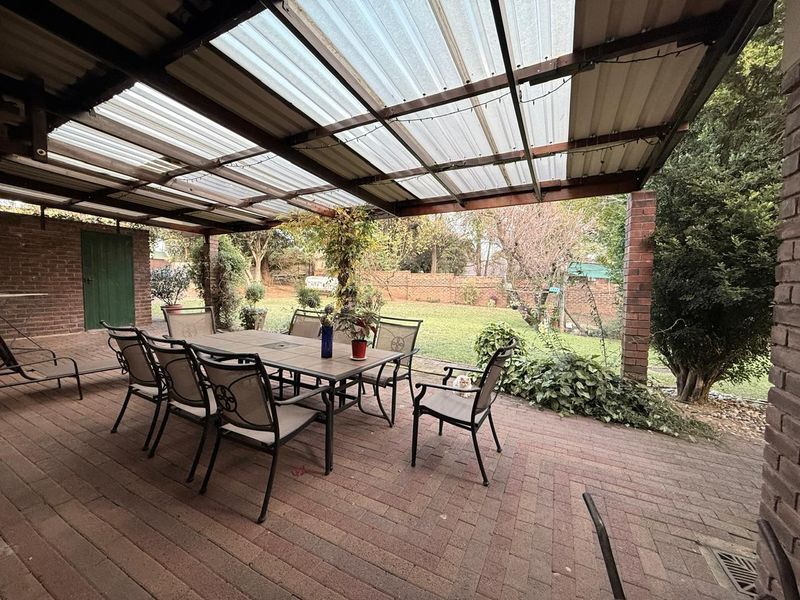 Covered outdoor patio area featuring brick paving, exposed timber rafters, and a corrugated roof, overlooking a private garden space.