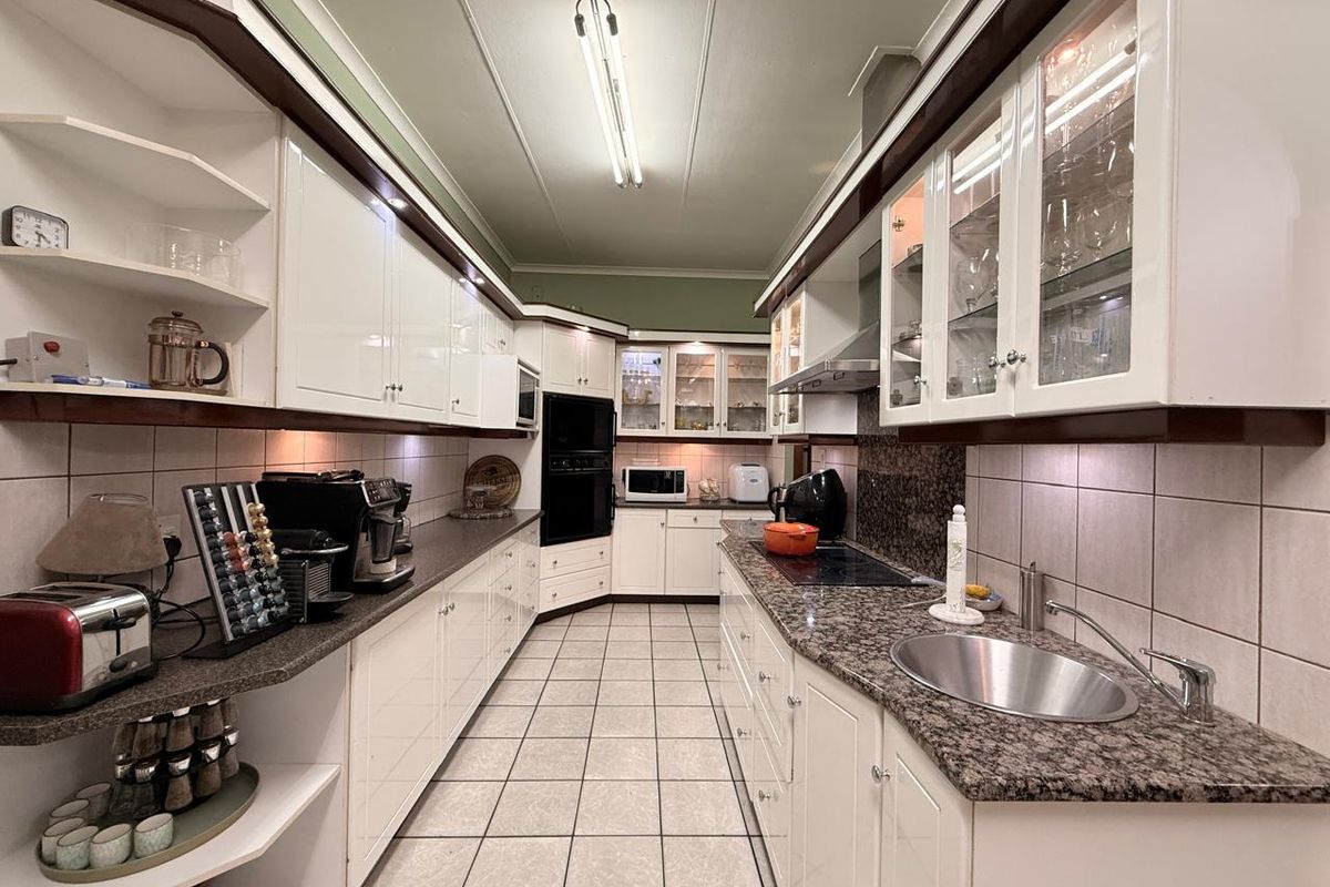 A functional galley-style kitchen featuring granite countertops, ample cabinetry, built-in oven, electric hob, and tiled flooring with integrated lighting.