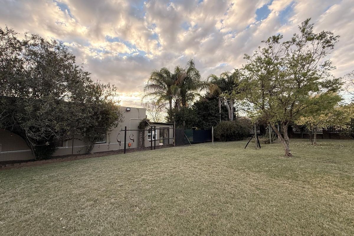 A spacious rear garden featuring a well-maintained lawn, mature trees, and perimeter fencing, providing a private outdoor area for the property.